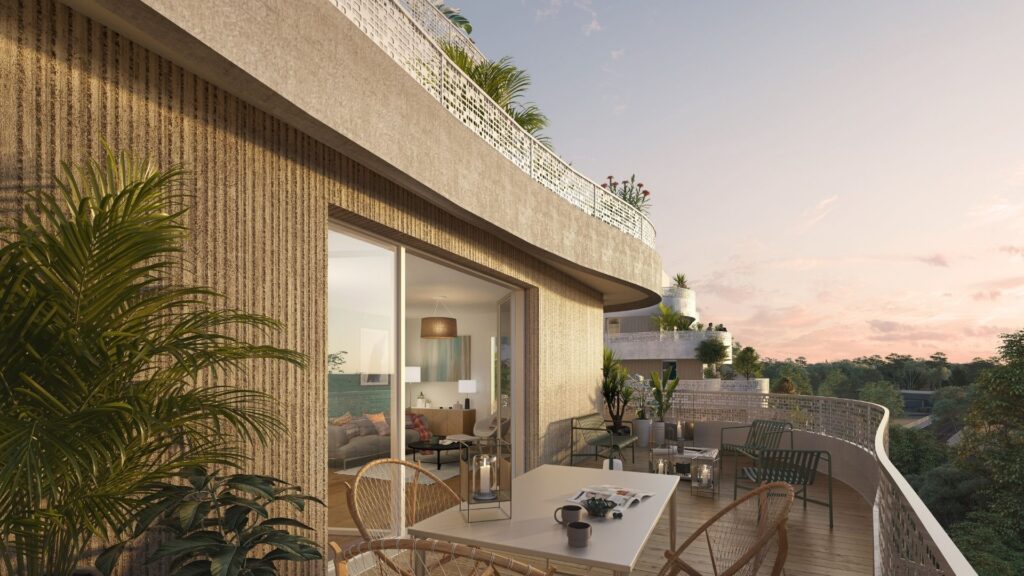 Vue rapprochée d'une large terrasse ensoleillée avec garde-corps en métal perforé, montrant un séjour lumineux en arrière-plan et une vue dégagée sur la végétation environnante